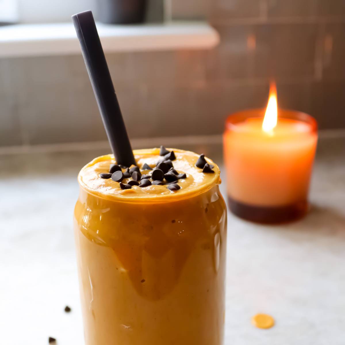 Pumpkin Smoothie with Straw in Glass Cup with Candle in Background