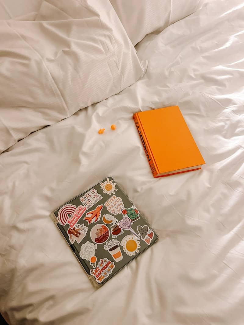 Laptop, book, and some treats on a bed.