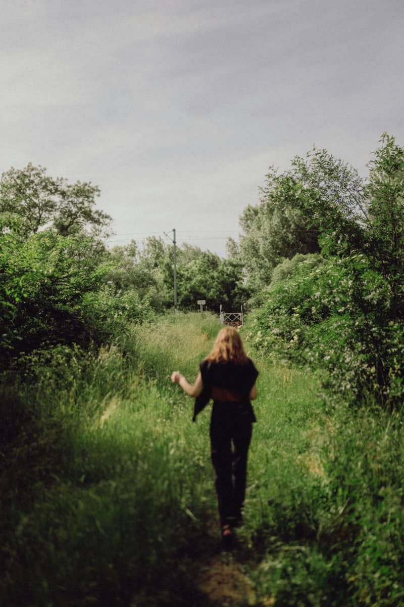 Woman walks through a grassy path in nature.
