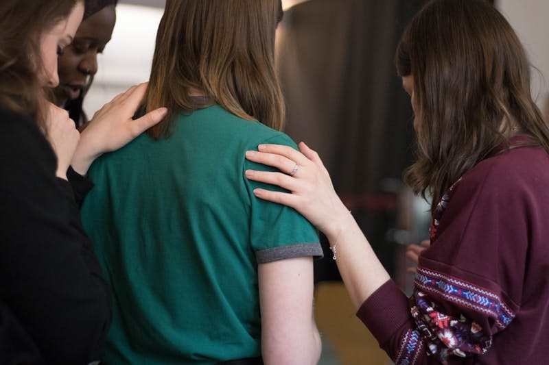 person wearing pink crew-neck shirt with hand clasped together