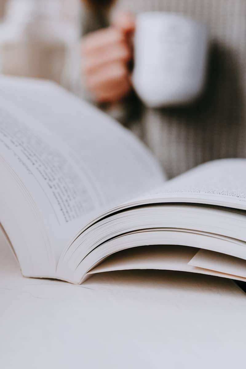 A person holding a cup of coffee while reading a book