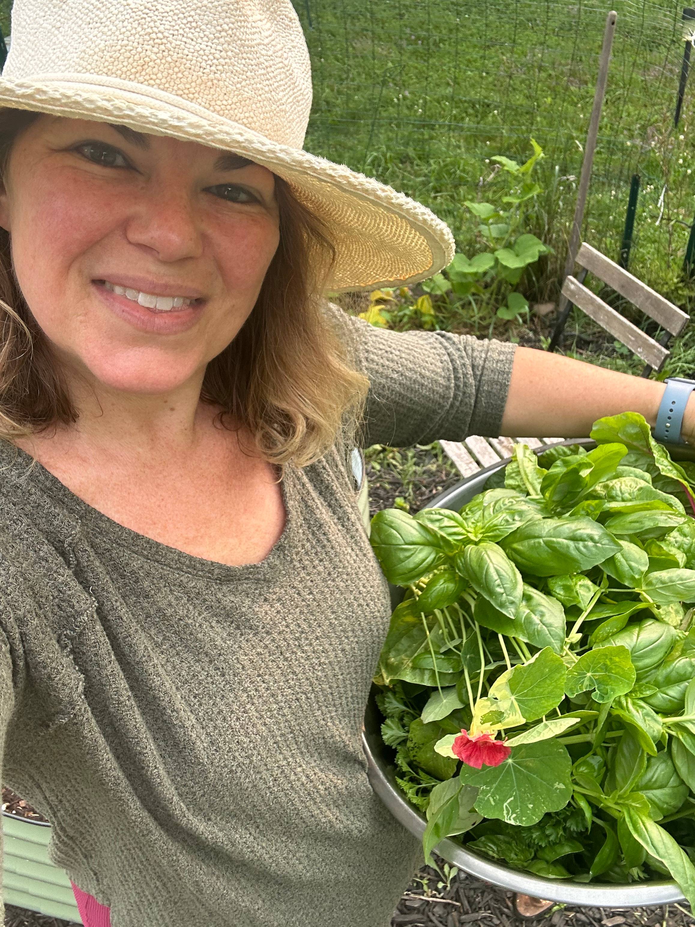 Deborah in the garden holding a giant bowl of leafy greens. 