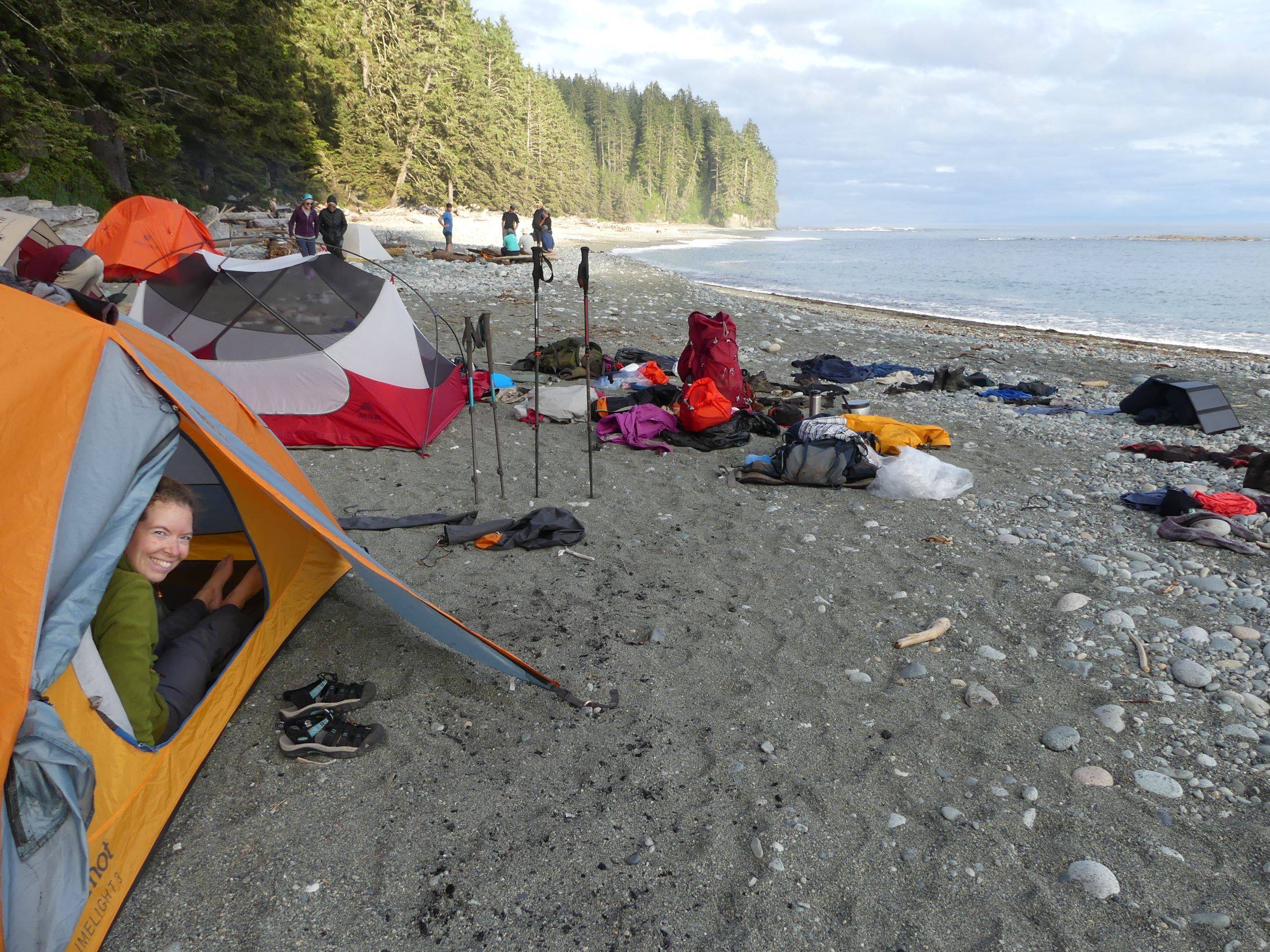 lady in a tent with gear scattered all over the sand beside the ocean