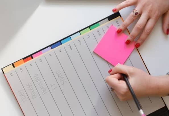 person holding pencil and stick note beside table
