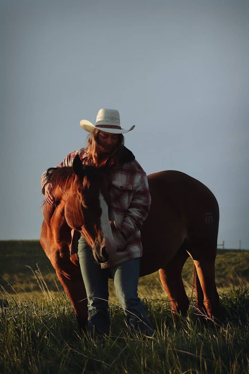 A cowgirl embraces her horse in a field.