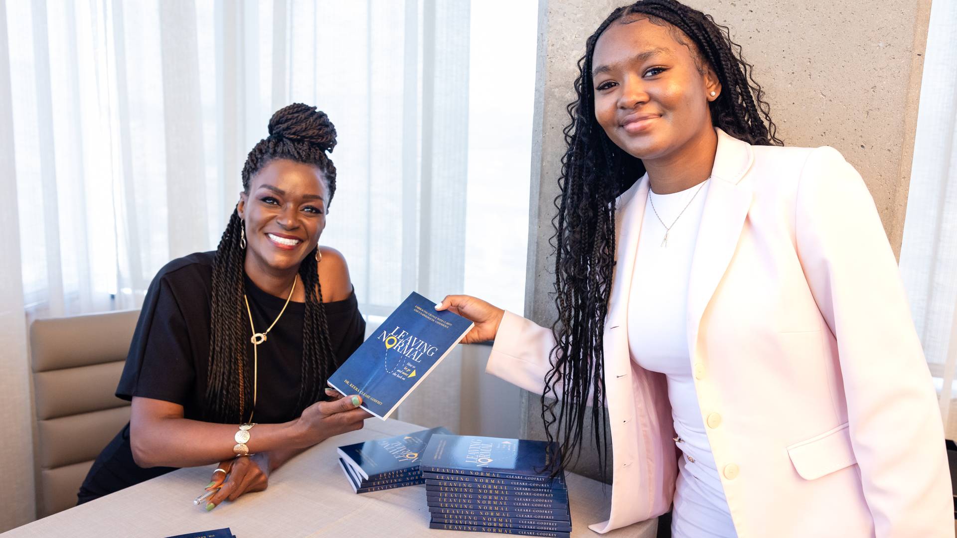 a picture of a young lady in a pink blazer with white top holding the book Leading Through Change with the author Dr. Keera Godfrey wearing a black top.