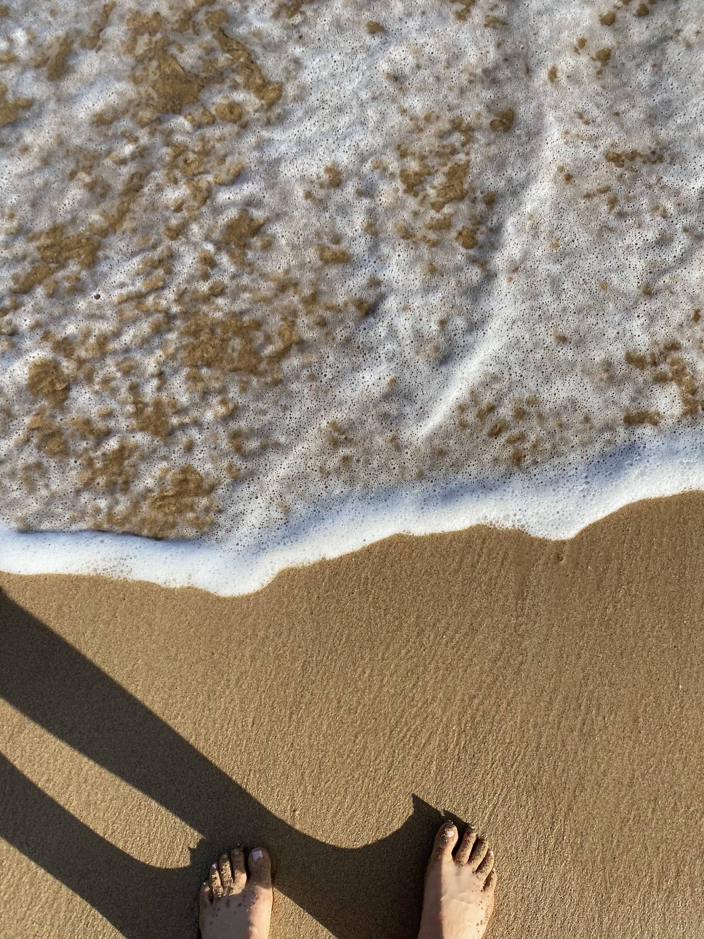 My bare feet on a sandy golden beach, a small wave coming in