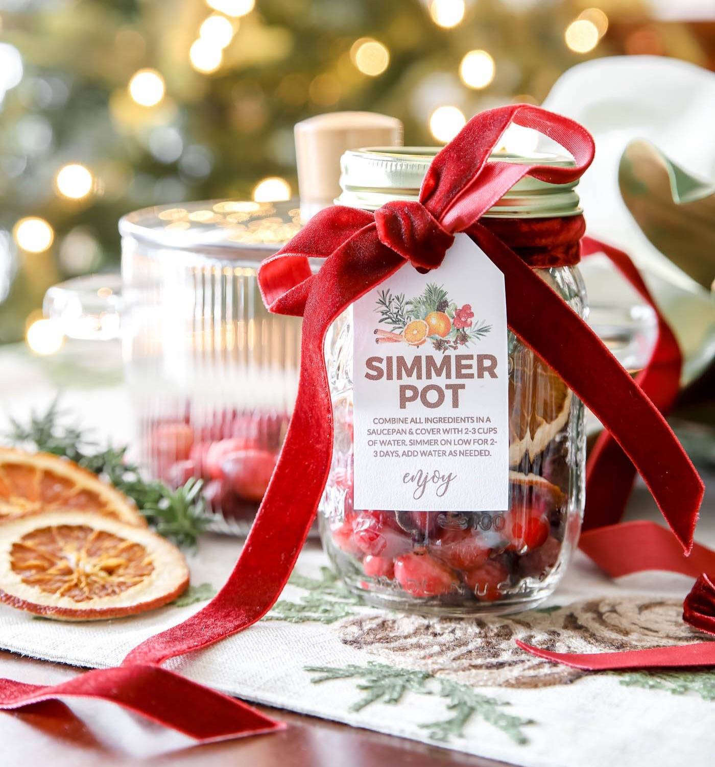 Christmas simmer pot recipe in a glass jar in front of a Christmas tree, including a gift tag printable. 