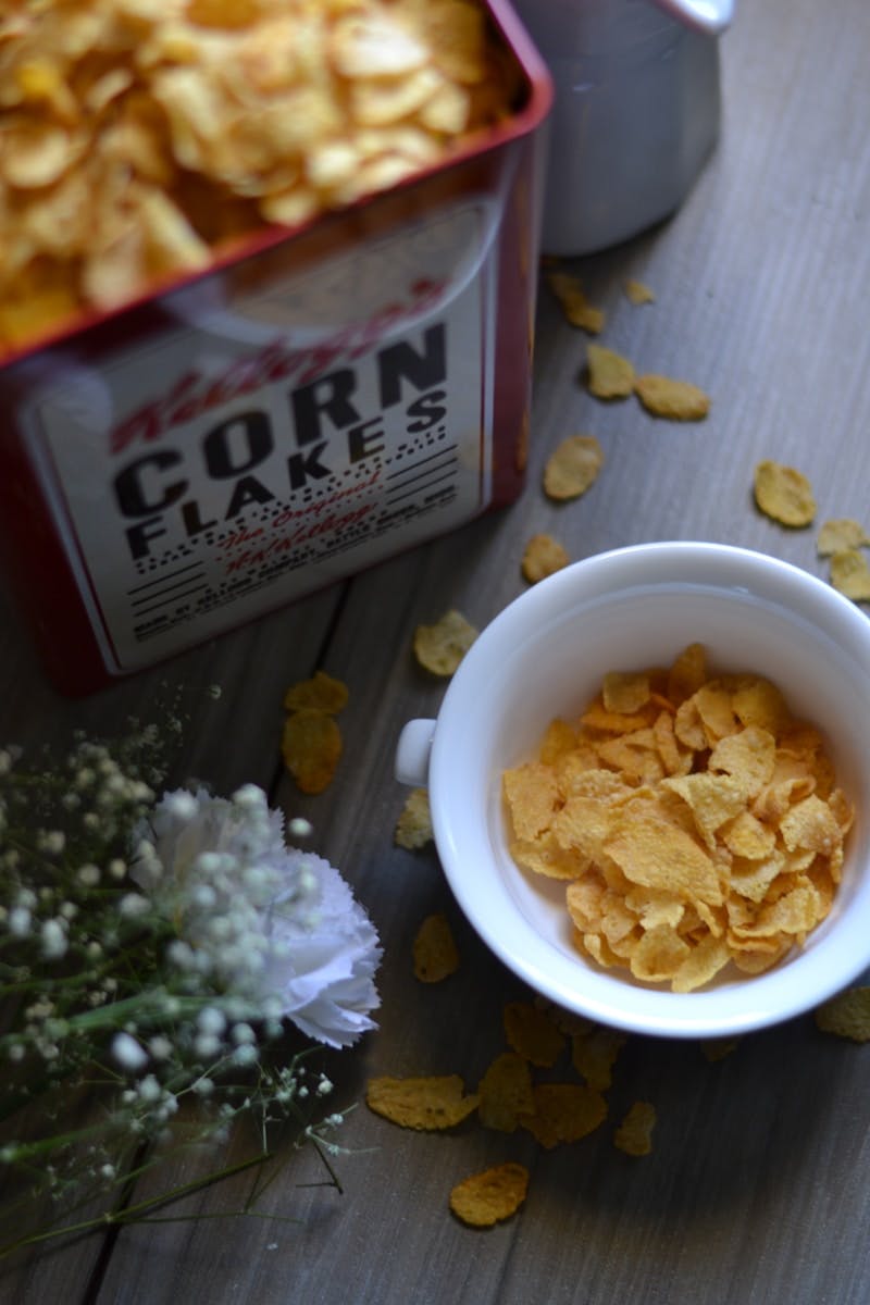 A bowl of corn flakes next to a can of corn flakes