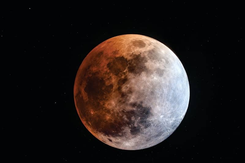 A blood moon lunar eclipse against a starry night sky.