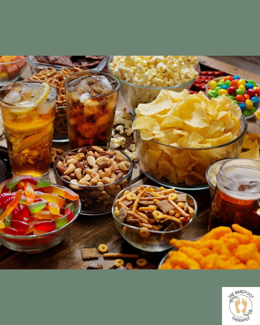 Assorted snack foods and drinks arranged on a table, including chips, popcorn, pretzels, candy, nuts, soda, and tea.