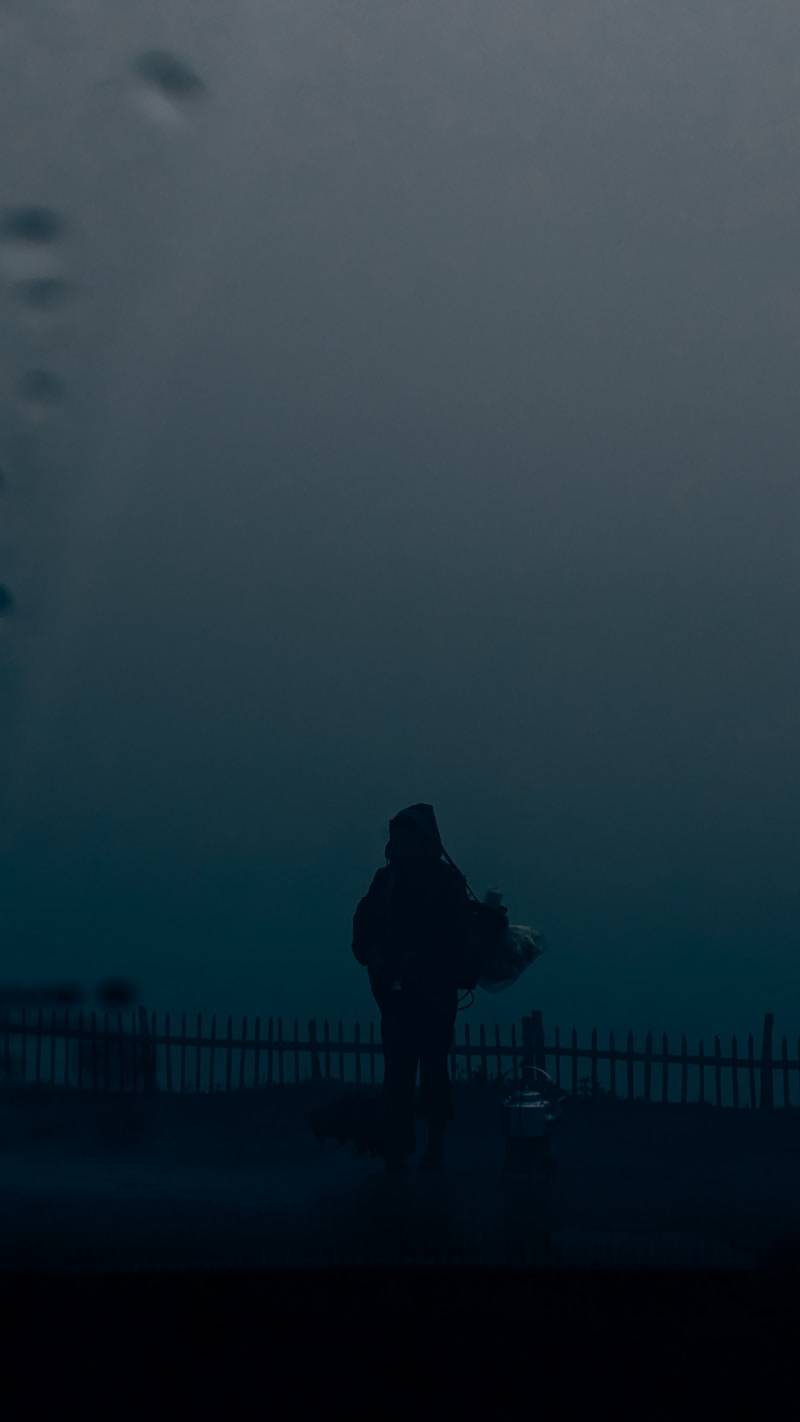 A person standing on a sidewalk in the dark