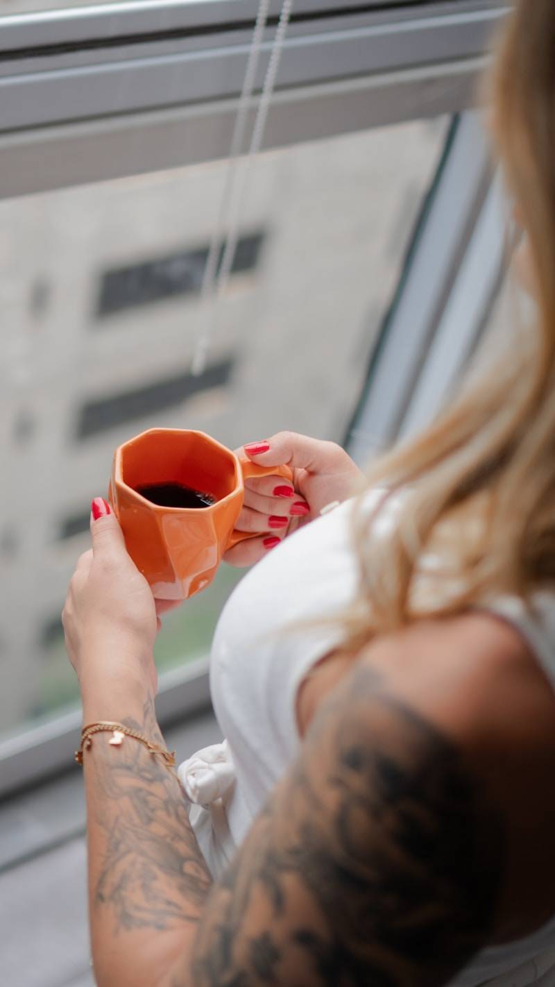 Woman holding an orange mug of coffee by the window