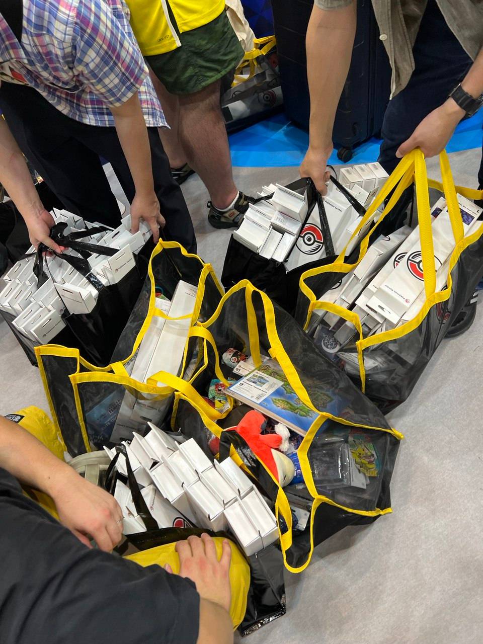 People carrying 5 shopping bags mostly filled with Pokémon trading card game playmats