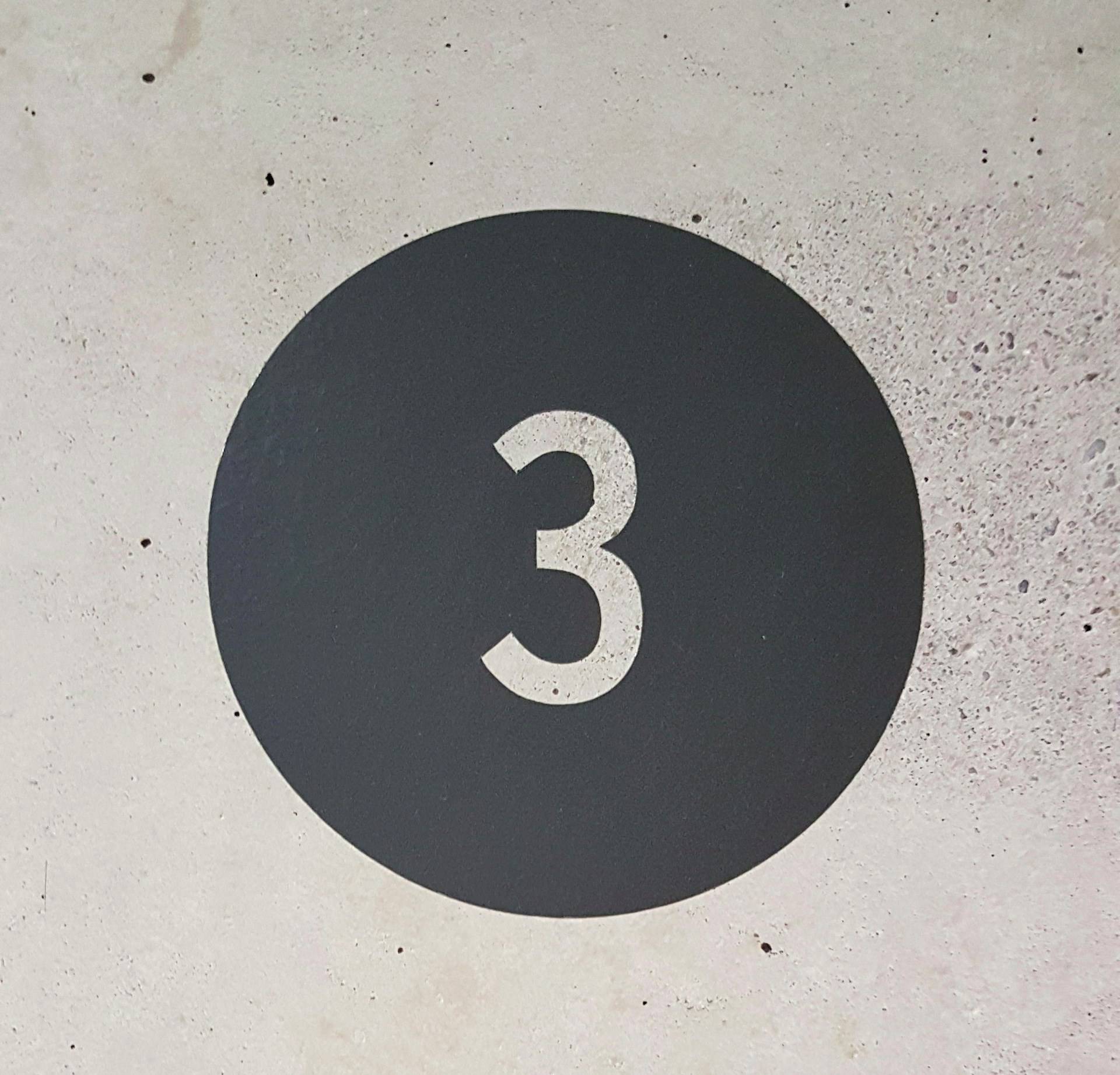 The number 3 against a dark grey circle on a grey wall