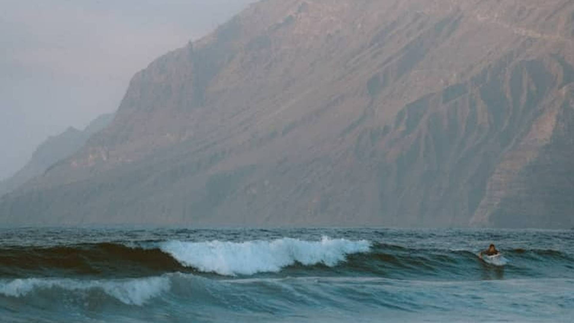 Waves crash in front of a misty mountain.