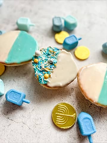 Hanukkah blue and white cookies scattered around dreidels and gelt.