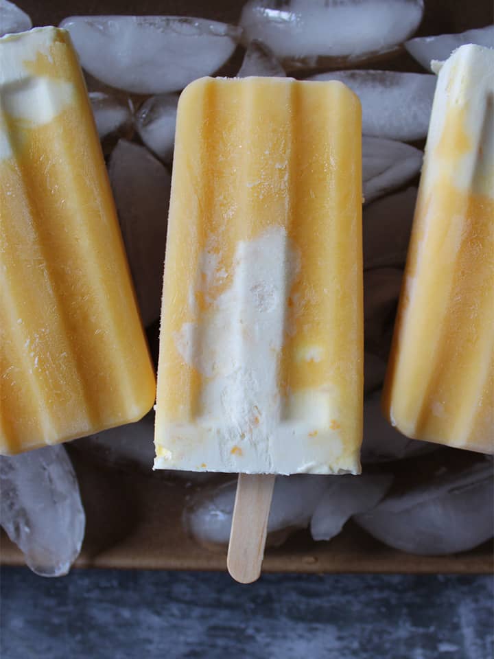 Orange creamsicle popsicle on a tray with ice cubes.	