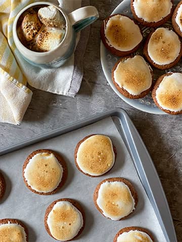 Hot chocolate cookies on a plate and sheet tray with a cup of hot chocolate on the side