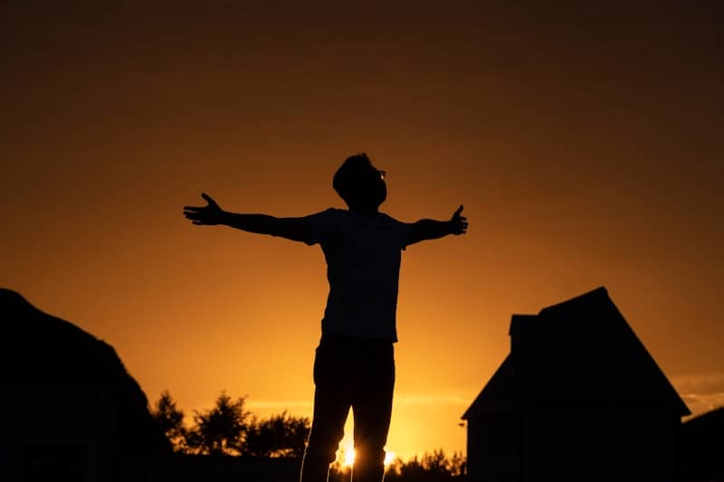 Man embraces the sunset with outstretched arms.