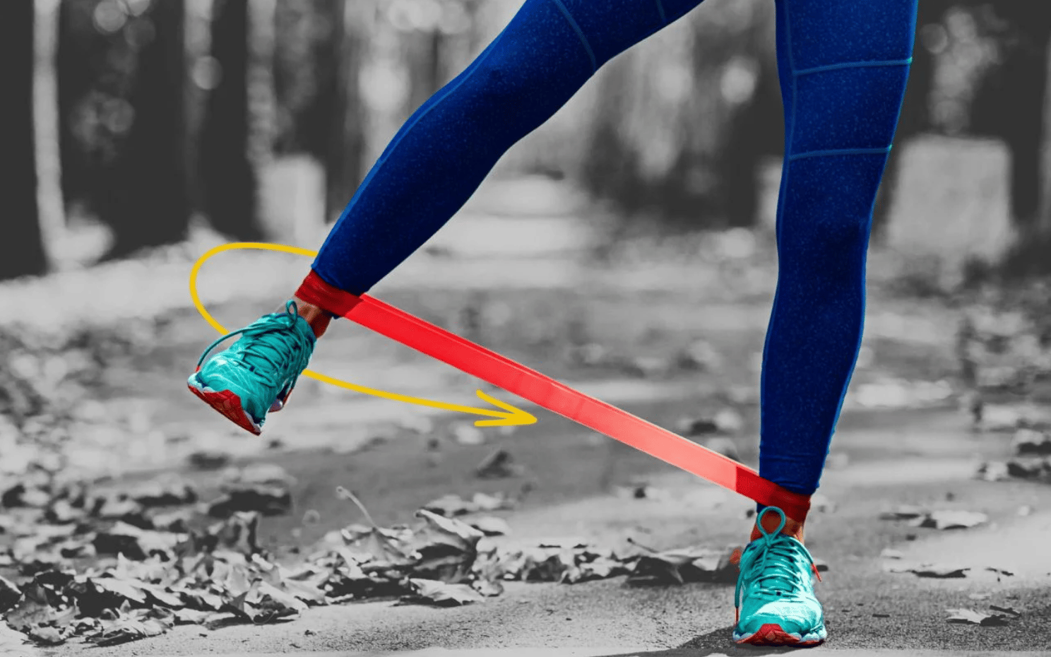 A person wearing blue leggings and turquoise sneakers is exercising outdoors with a red resistance band around their ankles. The person is lifting one leg to the side, demonstrating a lateral leg exercise. The ground is covered with fallen leaves, and the background is a blurred view of trees. A yellow arrow indicates the direction of the leg movement.
