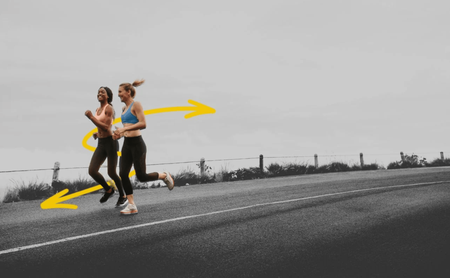 Two women are jogging on an empty road with a cloudy sky background. They are in focus with their colorful sportswear visible, while the rest of the image is in grayscale. Yellow arrows are drawn around them, suggesting movement. There is a fence and greenery in the background.
