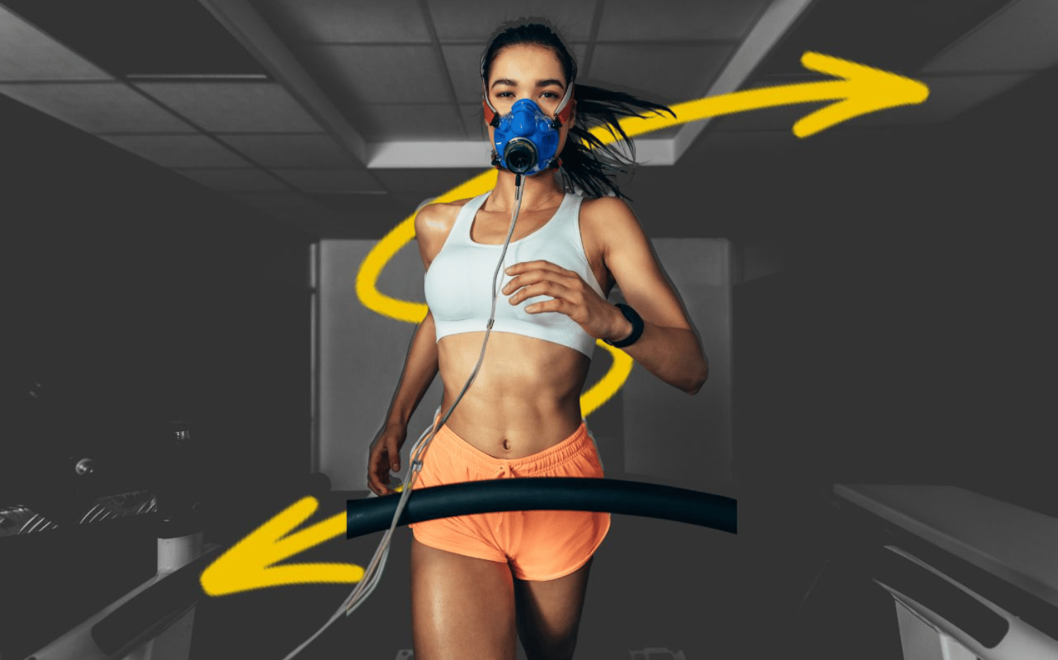 A woman running on a treadmill indoors, wearing a blue respiratory mask connected to a tube. She is dressed in an athletic outfit with a white sports bra and orange shorts. Yellow arrows are drawn over the image, indicating movement or direction. The background is dimly lit, highlighting her as the main focus.