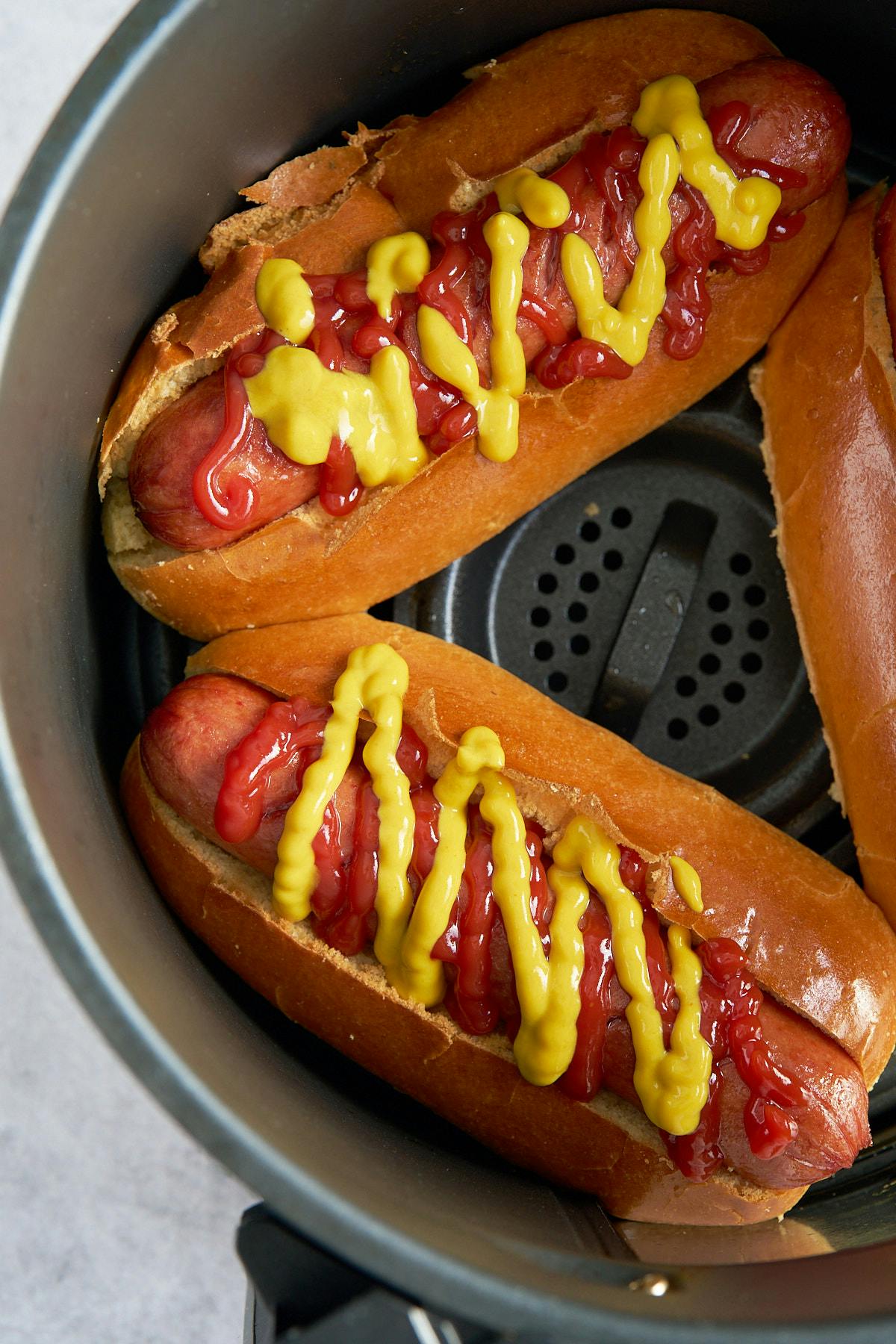 hot dog in air fryer basket with ketchup and mustard on it