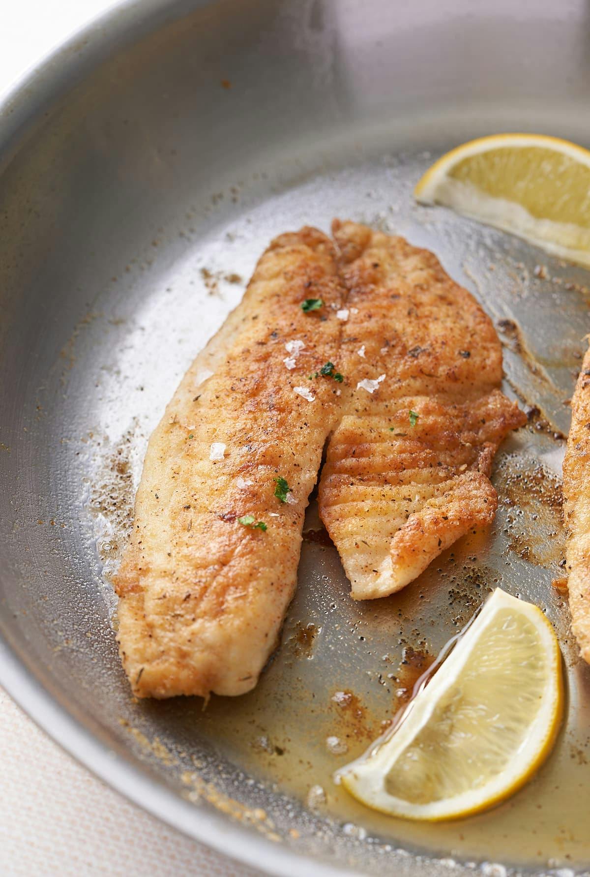 fried fish in skillet with lemon on side