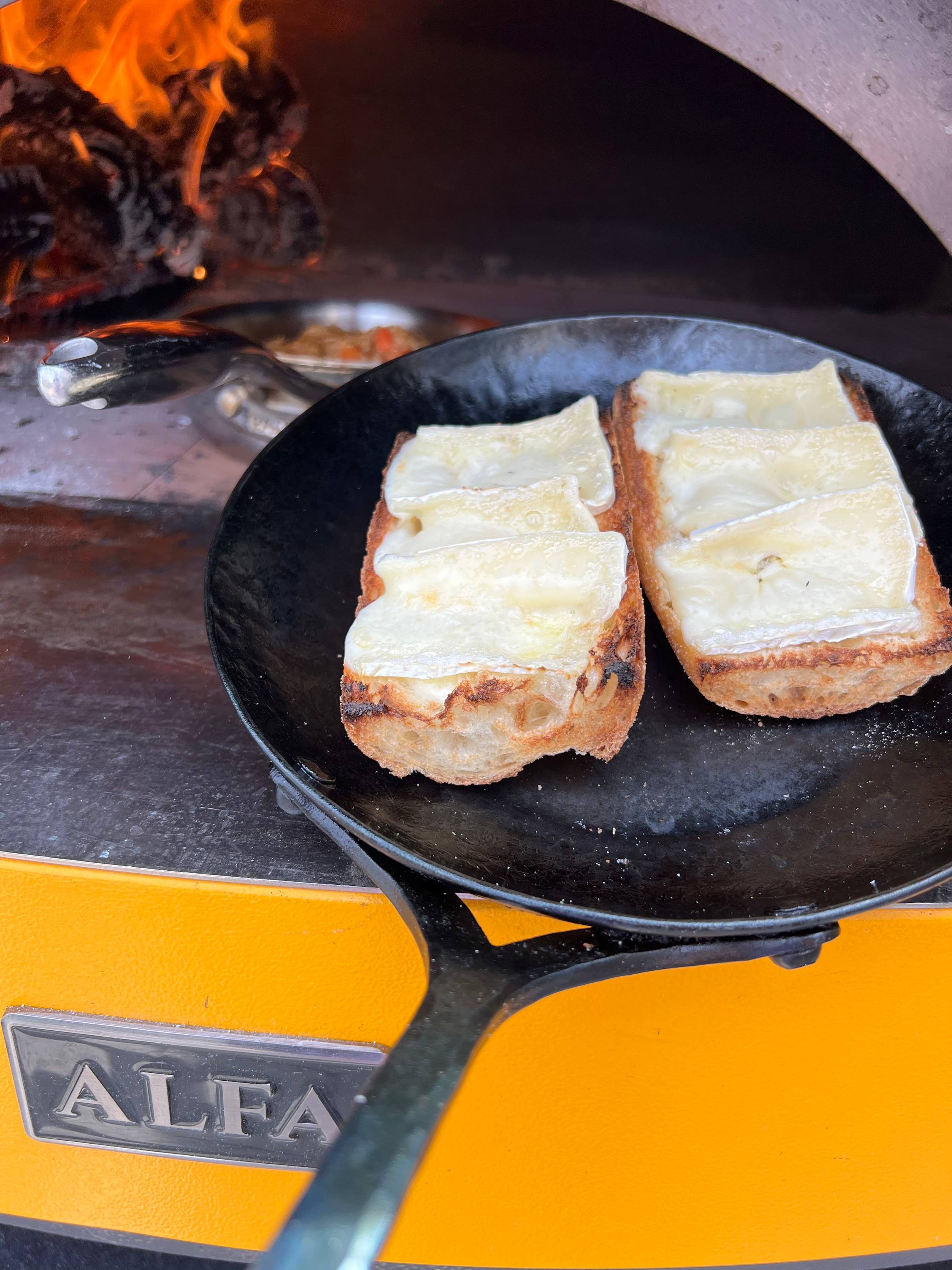 a pan with baguette and brie toasted in front of a wood oven 
