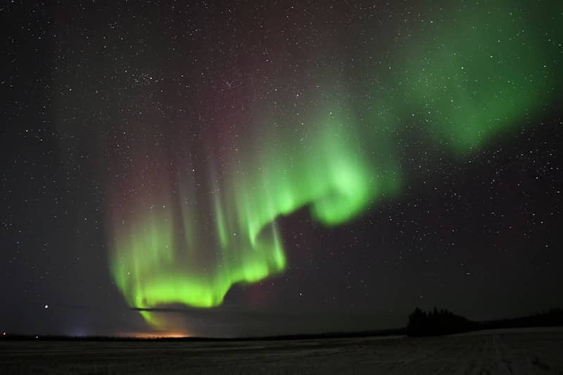 Green and purple aurora borealis over a dark landscape.