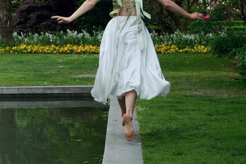 A woman in a white skirt and green top balancing on a stone ledge