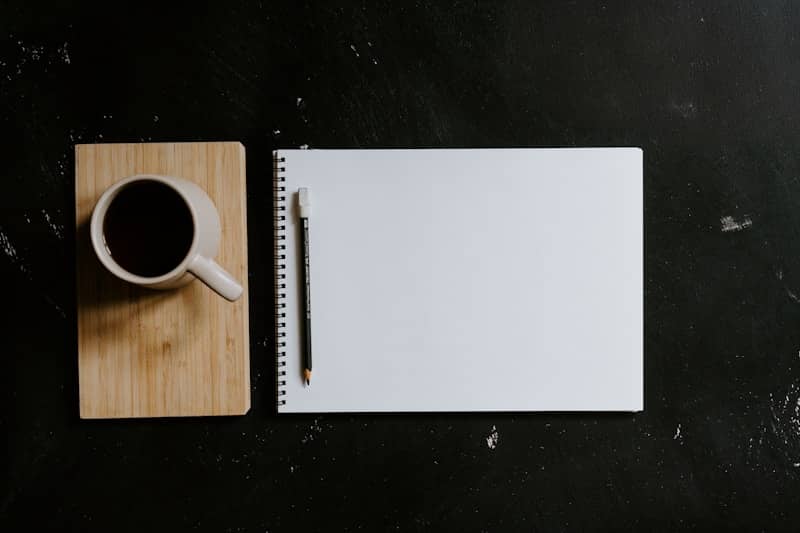 A cup of coffee and notebook with pen on desk