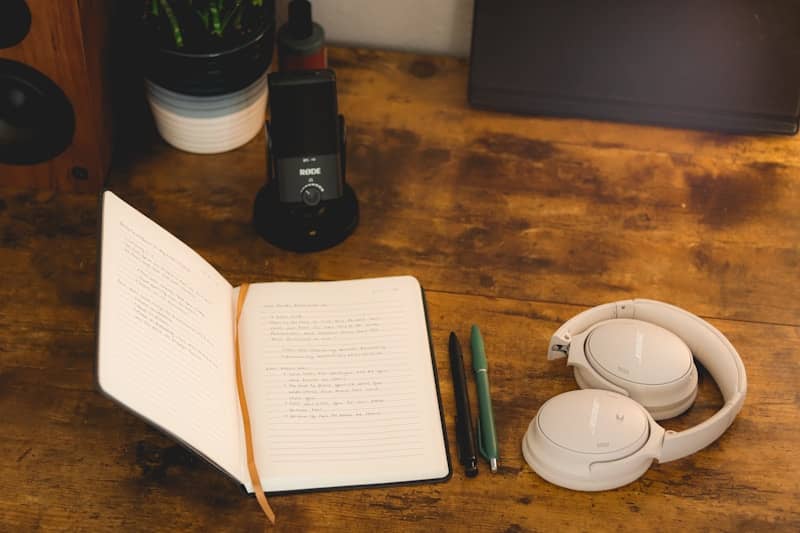 Open notebook, pens, and headphones on a rustic wooden desk.