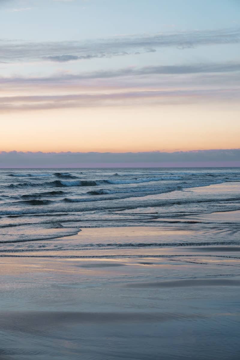 A person walking on the beach carrying a surfboard