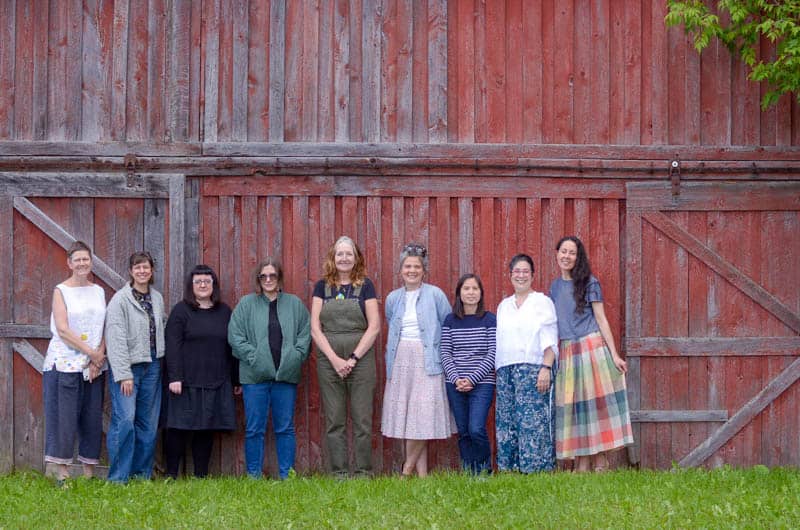 group of women in handmade outfits in front of a red barn
