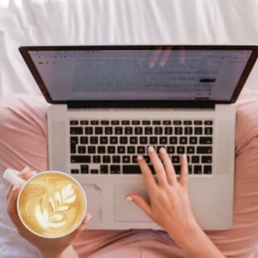 person using MacBook Pro and holding cappuccino
