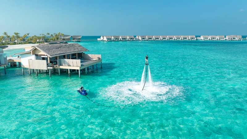 People enjoy watersports near overwater bungalows.