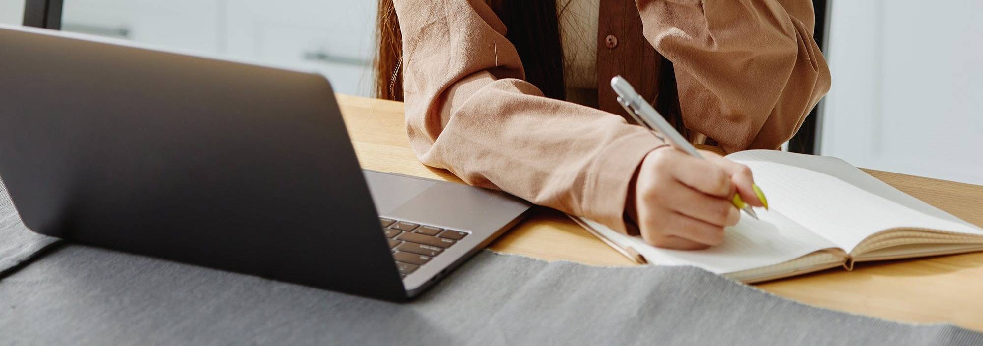 a laptop and a person writing on paper