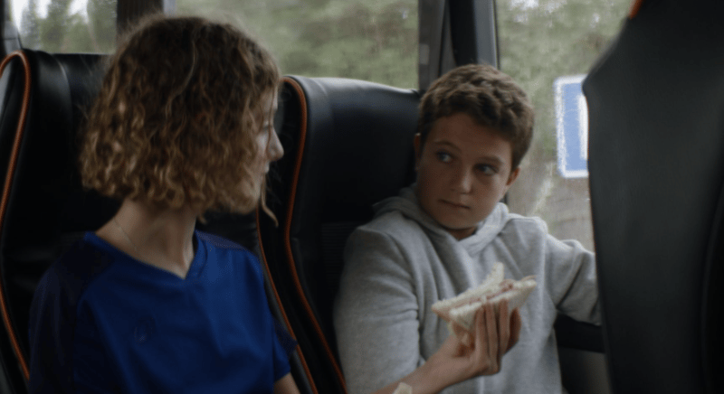 Extrait de la campagne de la marque Président. Une jeune femme et un garçon sont assis côte à côte dans un car. La jeune femme tend son sandwich au garçon.