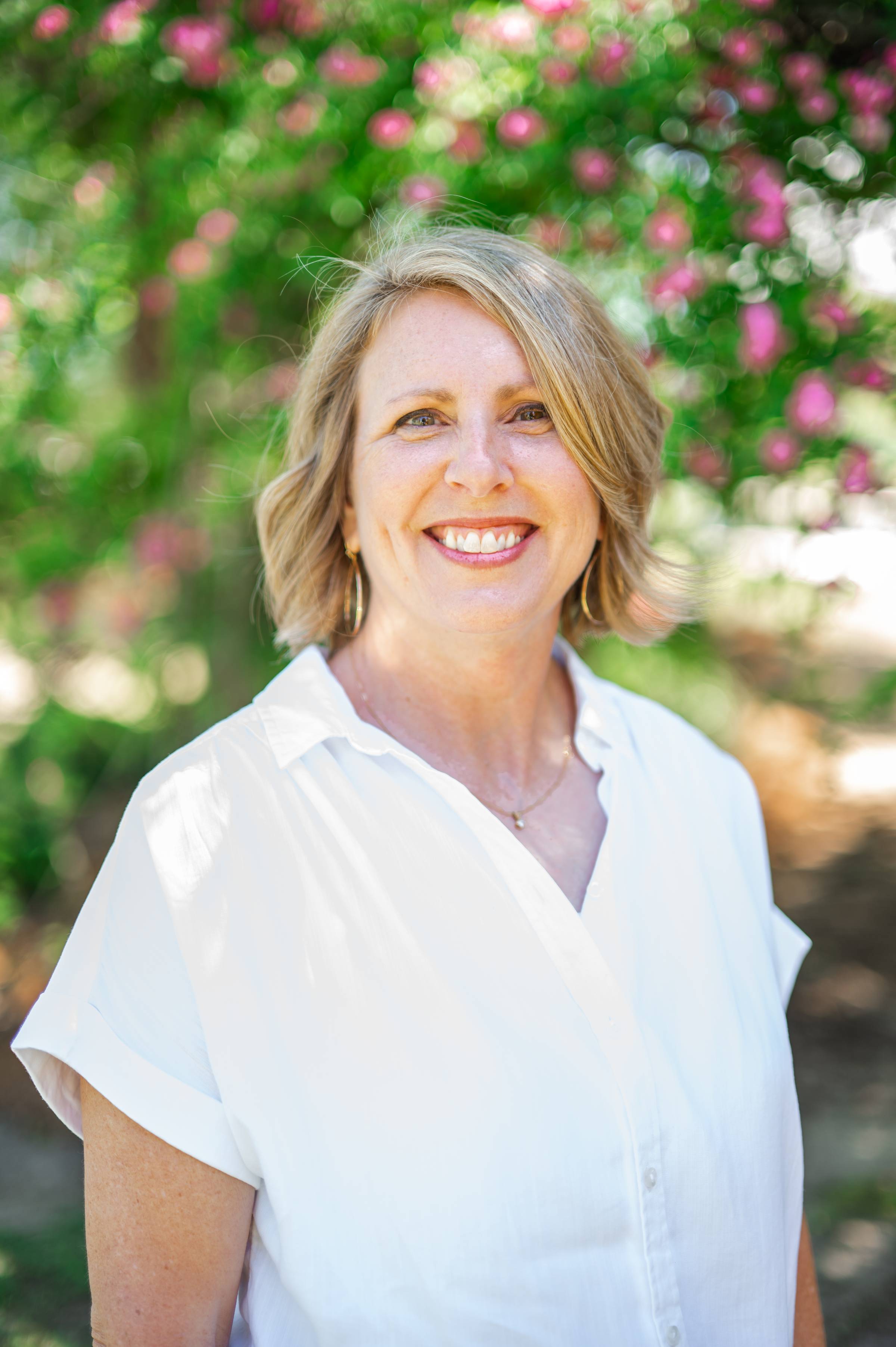 Christy Miller Bell standing outside under flowering tree wearing white shirt.