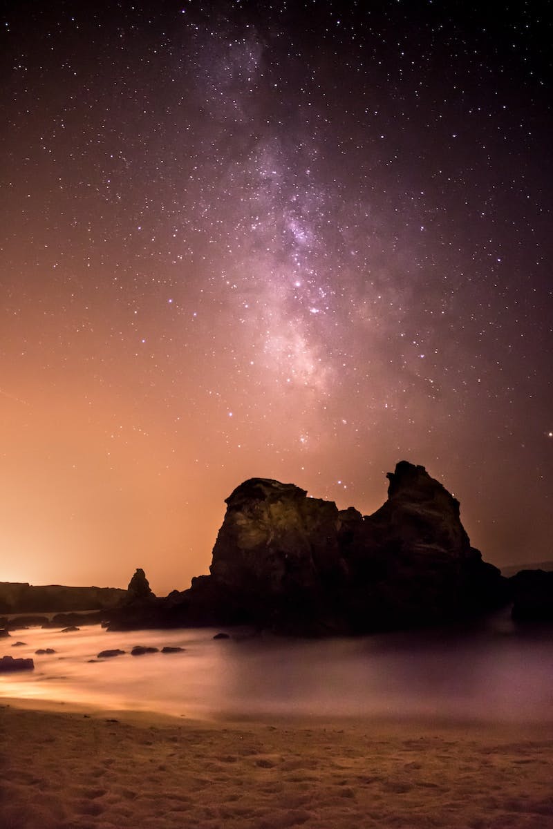 rock formation surrounded by water under black and white milky way