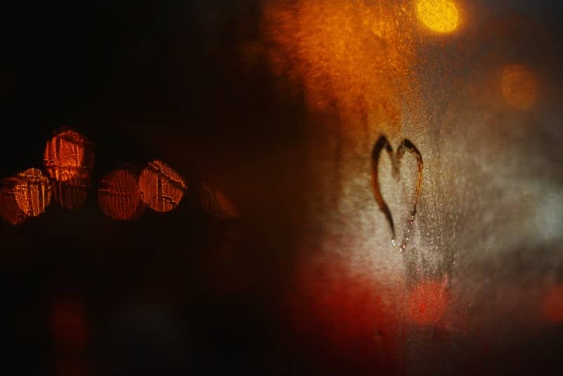 Heart drawn on steamy window with bokeh lights