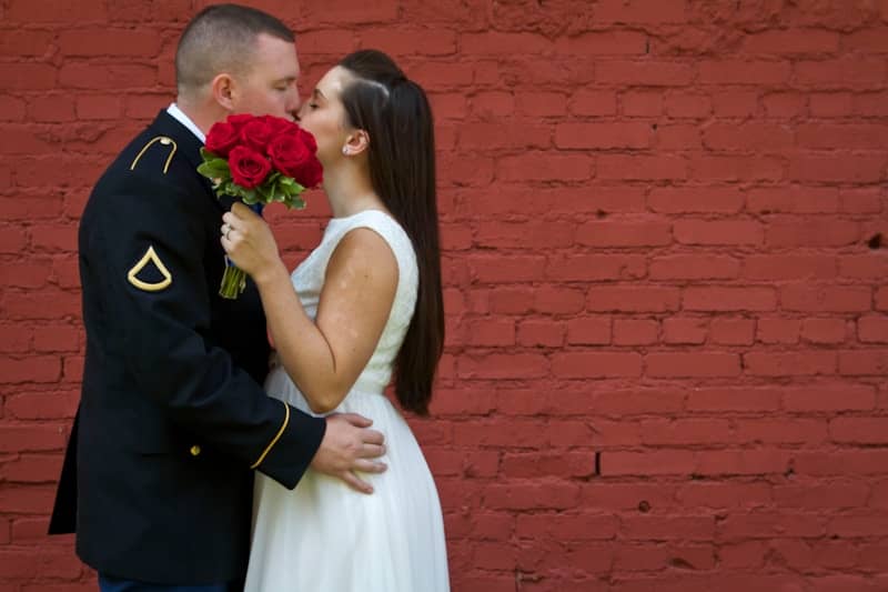 Soldier and bride kiss in front of red brick wall