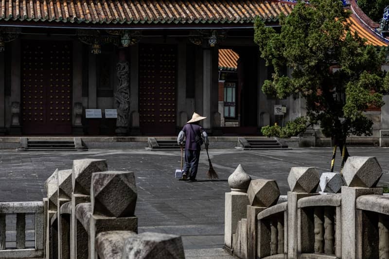 Person sweeping courtyard in front of traditional building