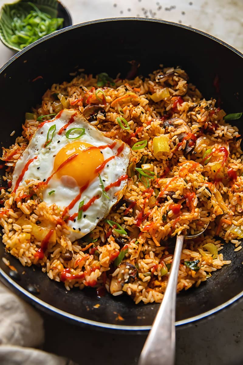 a black pan with fried rice topped by a fried egg with a serving spoon