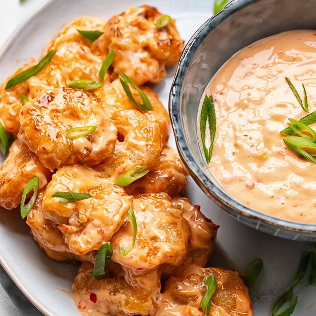 shrimp in sauce on a plate, with a bowl full of extra orange sauce