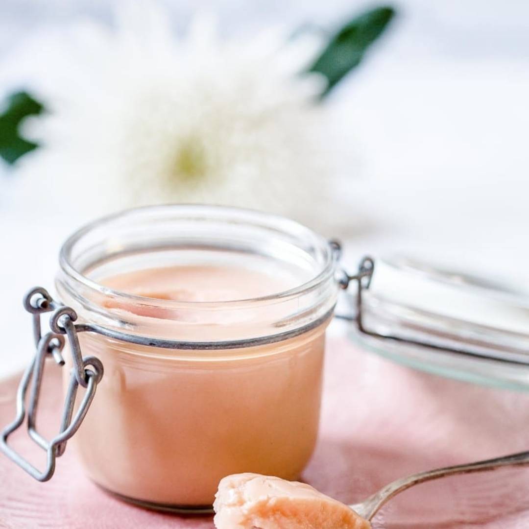 small jar with rhubarb curd on a pink plate, with a spoon serving next to it