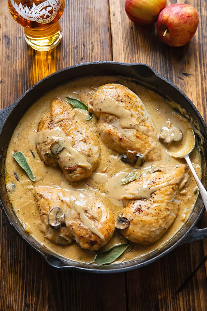 Cast iron skillet on a wooden background, with four chicken breasts in a creamy sauce.