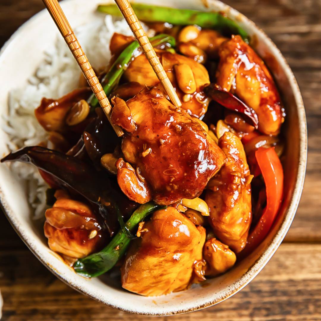 bowl of chicken on rice with a glaze, a piece being removed by chopsticks